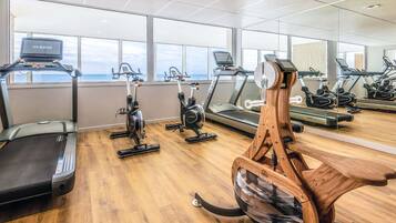 Une salle de sport équipée de nombreux appareils d’exercice, notamment des tapis de course et des vélos d’appartement, et dotée de grandes fenêtres laissant entrer la lumière naturelle.