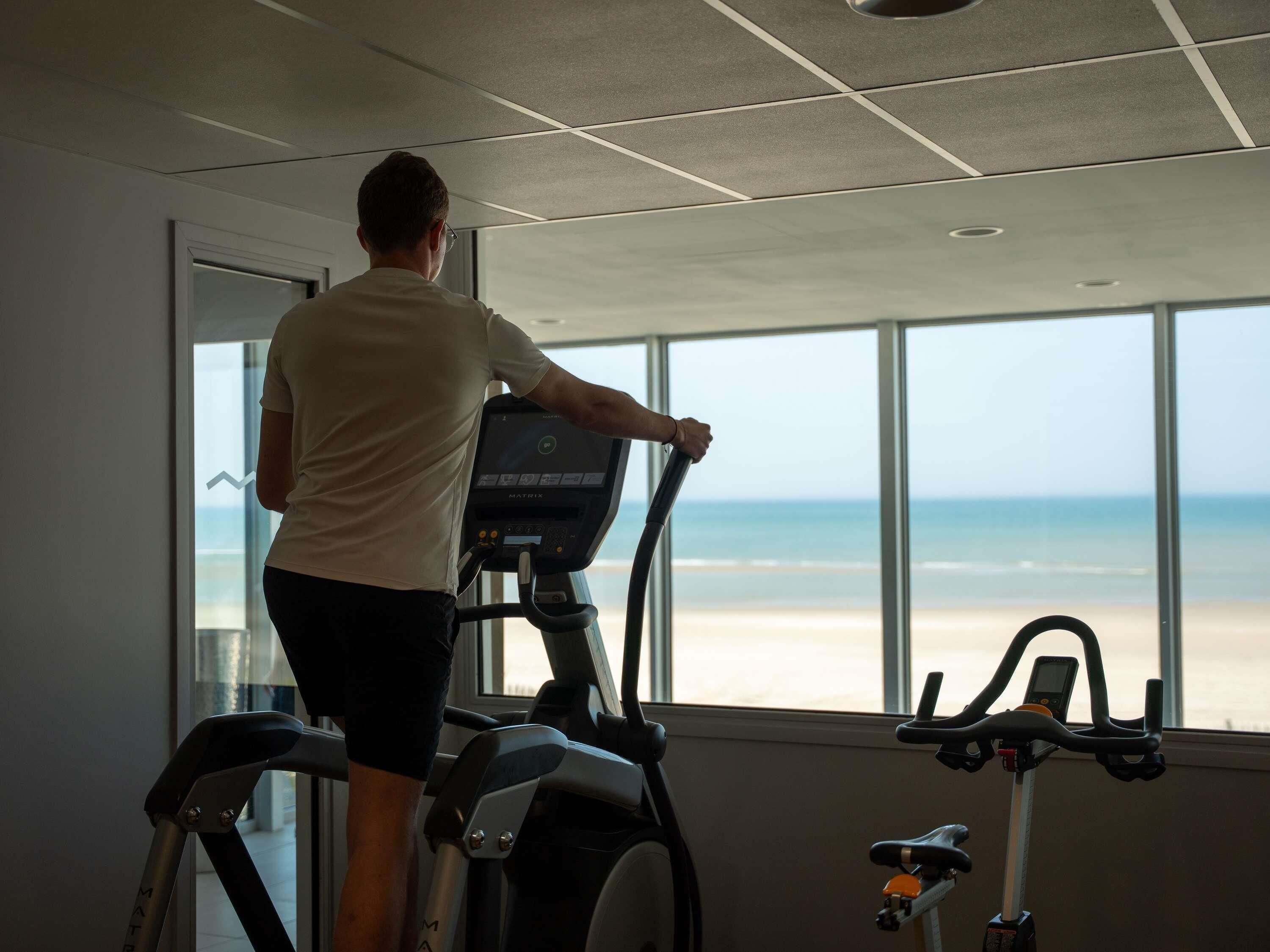 Una persona usando una máquina elíptica con vista a la playa a través de amplios ventanales.