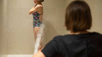 A person in a patterned swimsuit standing in a shower with water running.