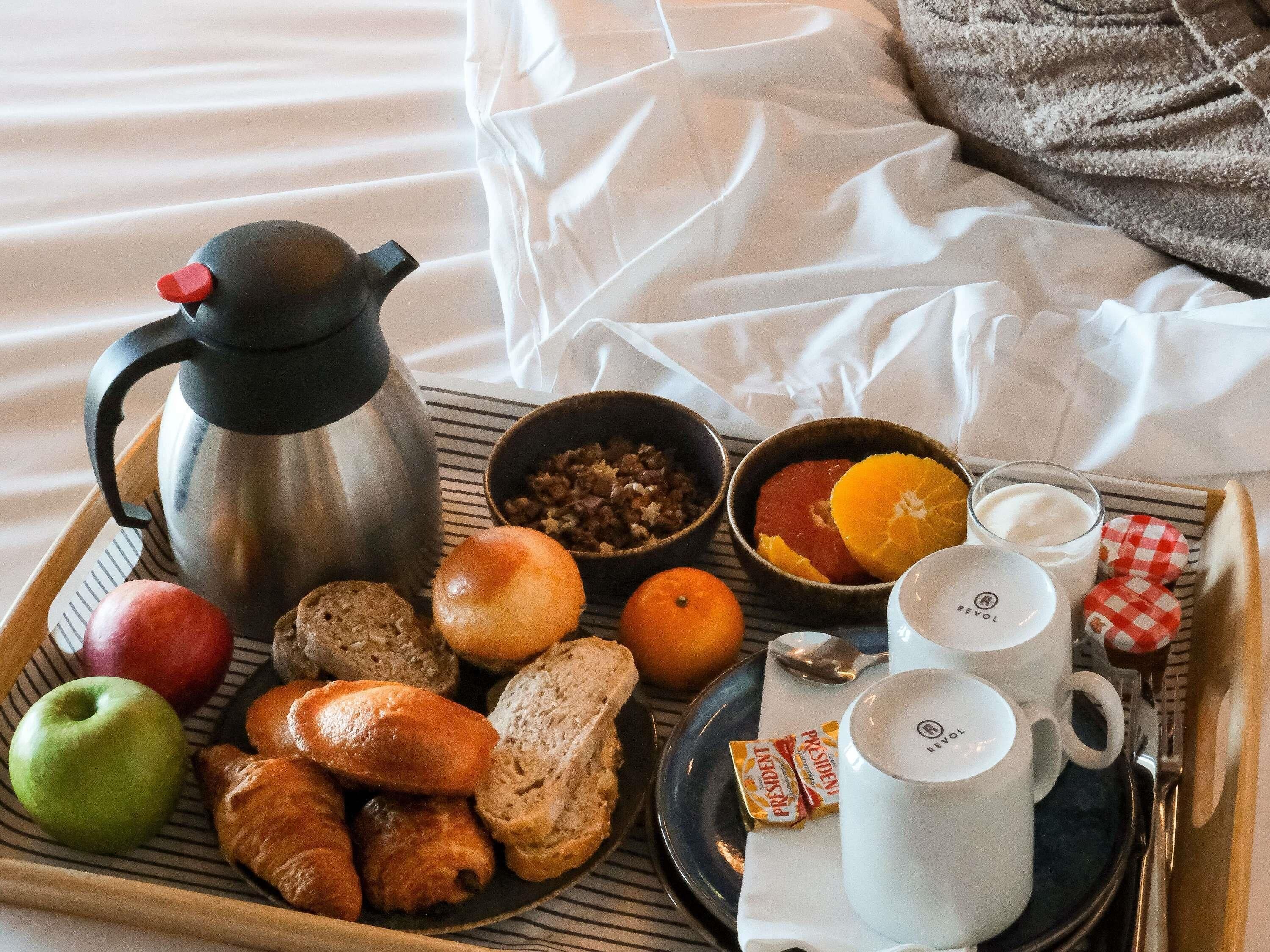 A breakfast tray with a coffee pot, bread, fruits, and a mug.
