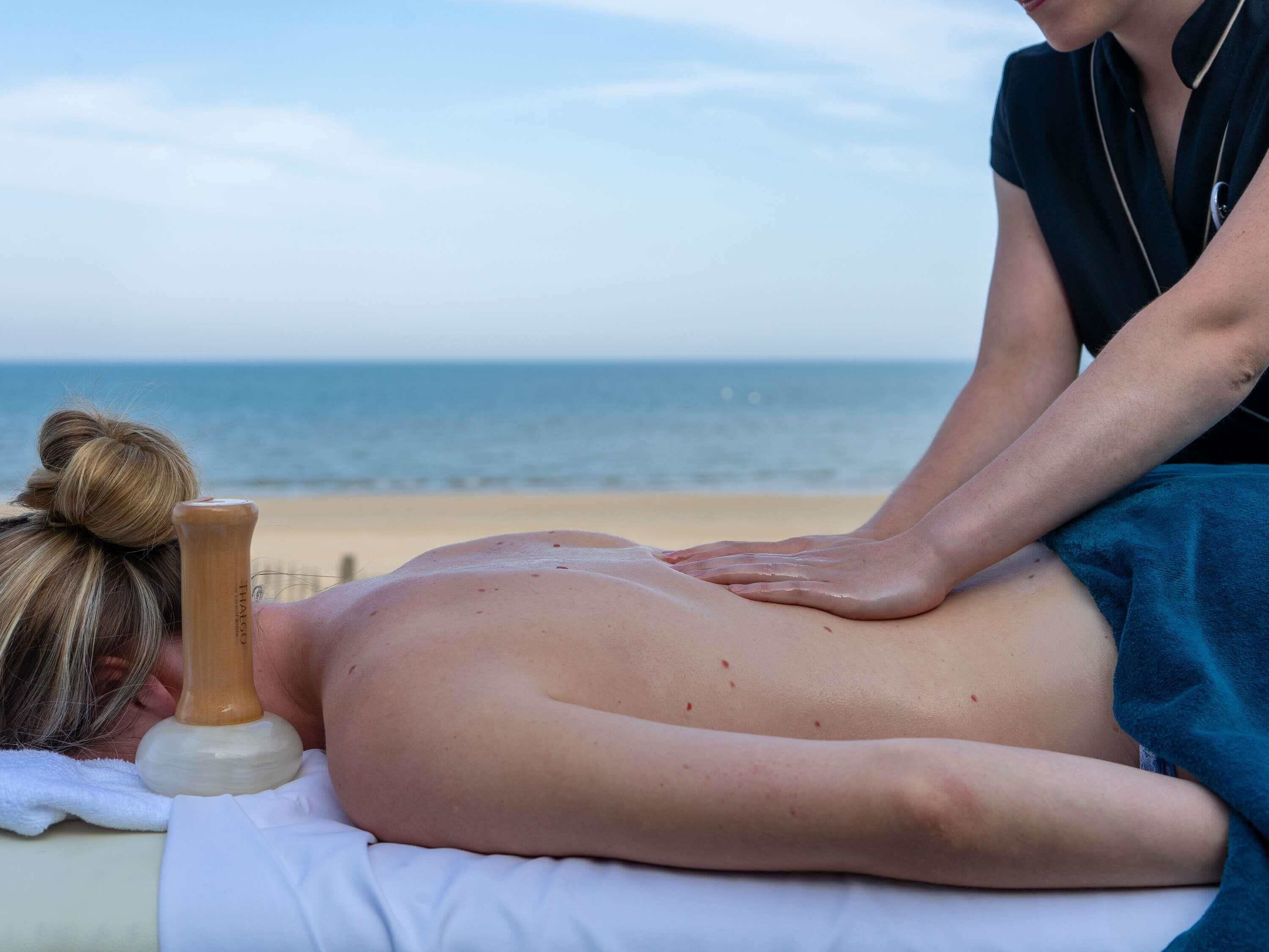 Iemand ontvangt een massage op het strand, met een handdoek en een massagewortel.