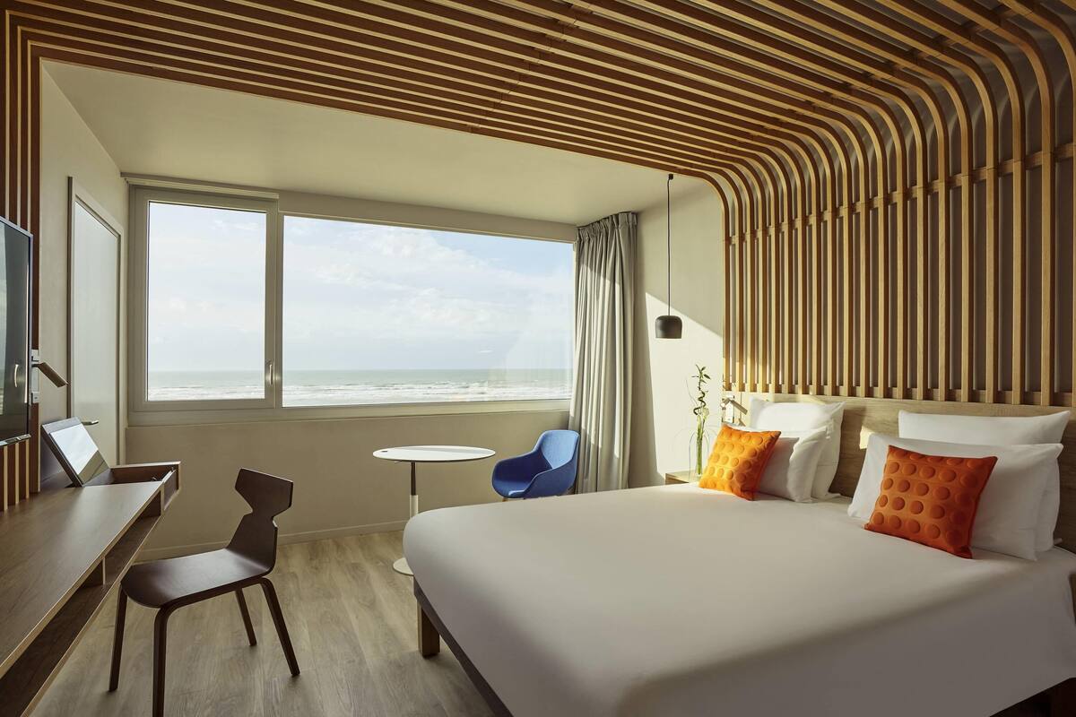 Ein Hotelzimmer mit einem großen Bett, einem Schreibtisch, einem Stuhl, einem kleinen Tisch und Blick aufs Meer.