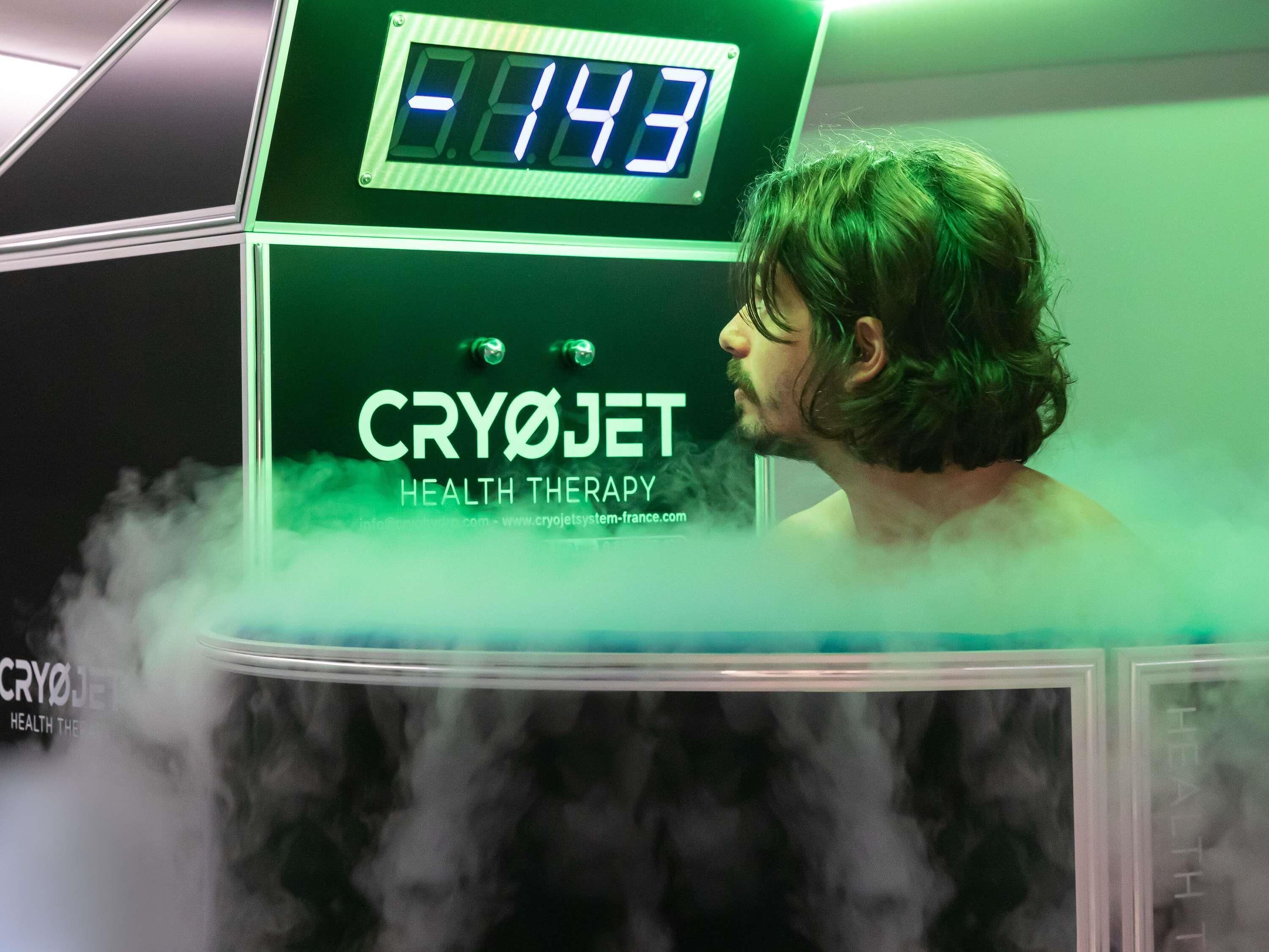 A person in a cryojet therapy chamber with a digital display reading 8.14.3.