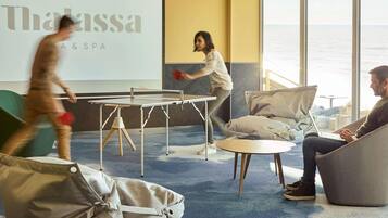 Un área lounge moderna con mesa de ping pong, asientos cómodos y una pantalla grande que muestra el nombre 'Thalassa SPA'.