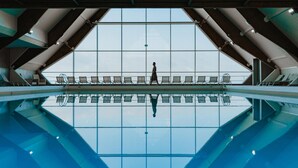 A swimming pool with a clear view of the sky through large windows, a person walking, and lounge chairs. - Novotel Thalassa Le Touquet Hotel (Le Touquet-Paris-Plage)
