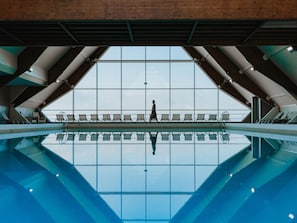 Une piscine avec de grandes fenêtres offrant une vue dégagée sur le ciel, une personne qui se promène et des chaises longues.