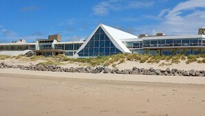 A modern building with a prominent triangular glass facade, situated on a sandy beach with a clear sky. - Novotel Thalassa Le Touquet Hotel (Le Touquet-Paris-Plage)