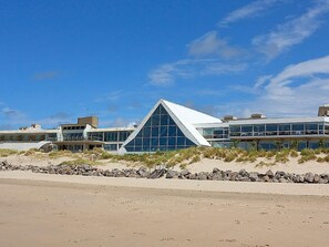 A modern building with a prominent triangular glass facade, situated on a sandy beach with a clear sky. - Novotel Thalassa Le Touquet Hotel (Le Touquet-Paris-Plage)