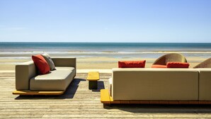 A beachside lounge with a wooden deck, two sofas with red cushions, and a small wooden table. - Novotel Thalassa Le Touquet Hotel (Le Touquet-Paris-Plage)