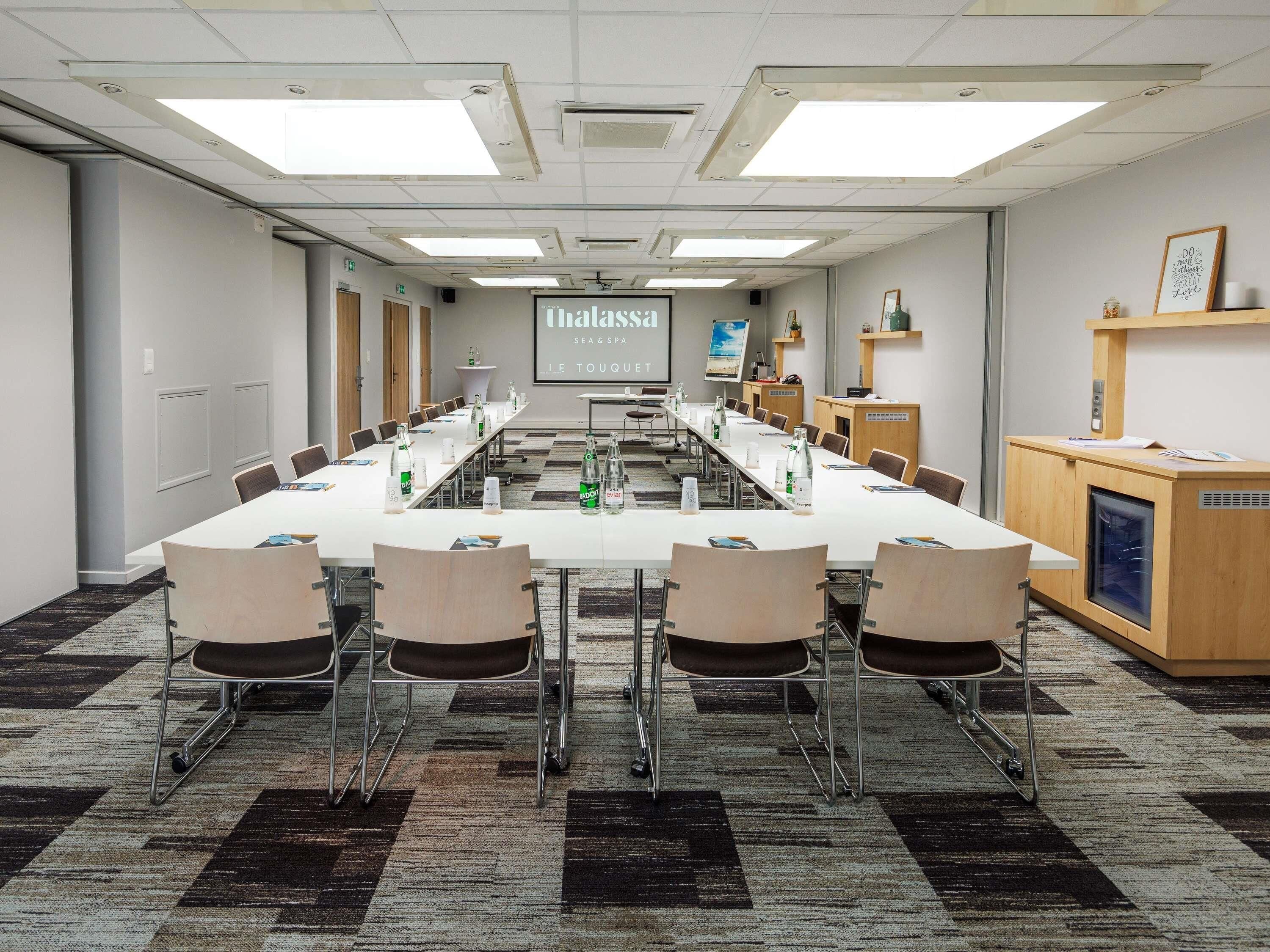 A conference room with a long table, chairs, a projector screen, and a presentation on the wall.