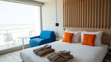 Habitación de hotel con cama, una silla azul, balcón y vistas, y cabecera de madera.