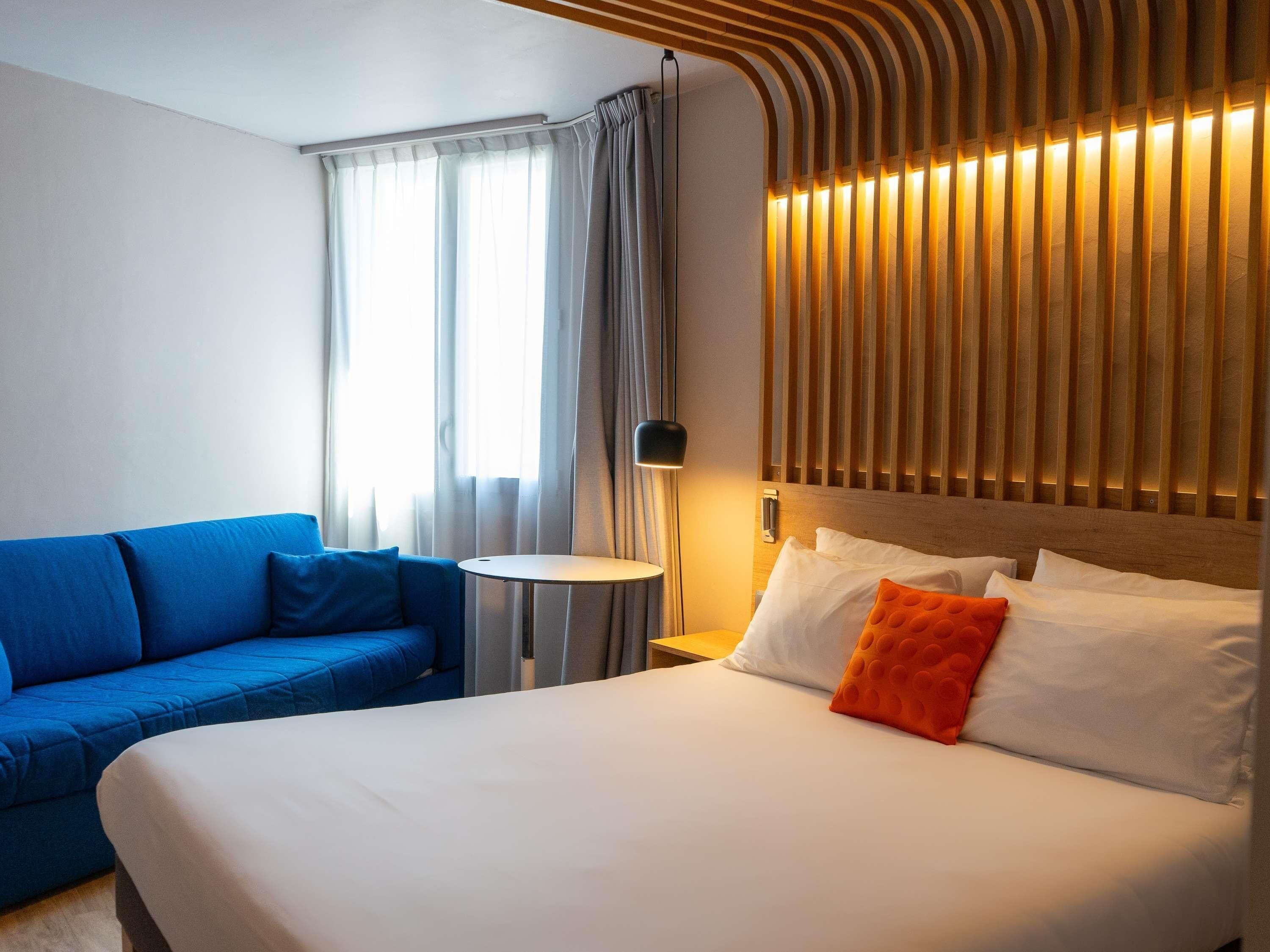 Una habitación de hotel con una cama, un sofá azul, una mesita redonda y una lámpara.