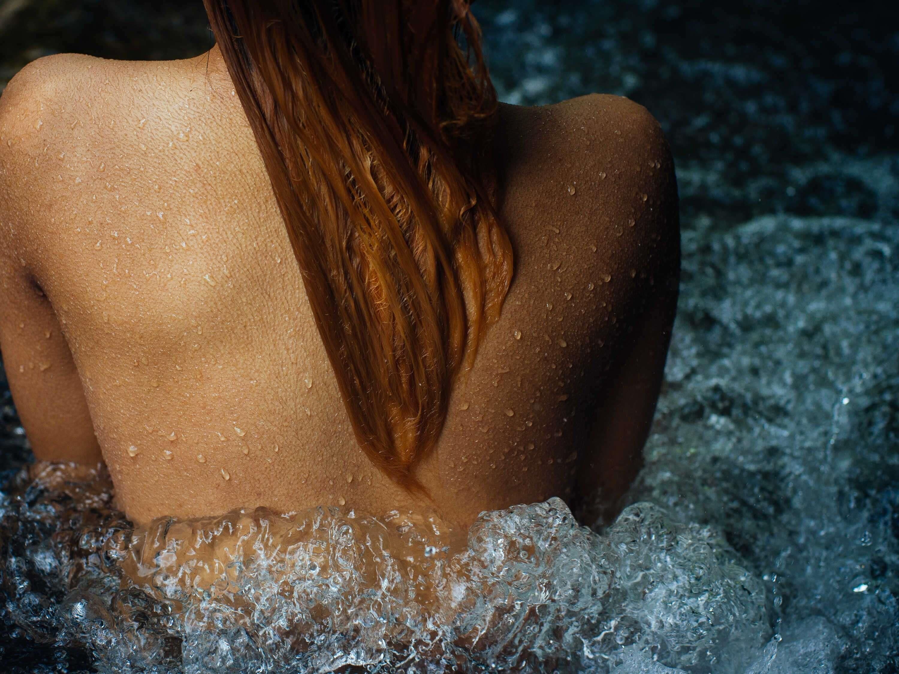 Eine Person mit langem Haar sitzt in einer mit Wasser gefüllten Badewanne.