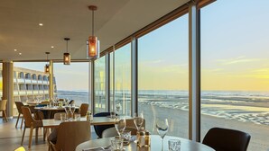 A restaurant with tables set for dining, large windows offering a view of the beach, and modern interior design. - Novotel Thalassa Le Touquet Hotel (Le Touquet-Paris-Plage)