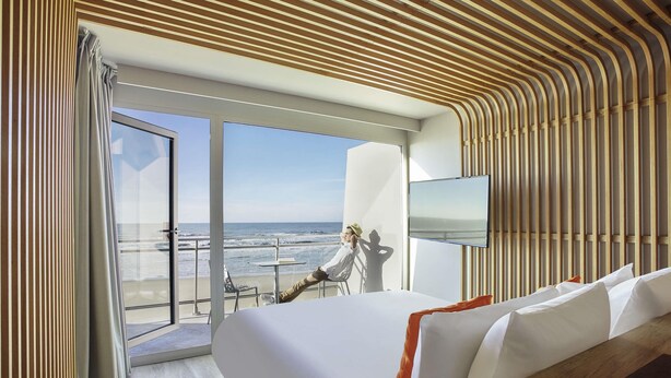 A modern hotel room with a large bed, a TV, and a balcony with a view of the beach. - Novotel Thalassa Le Touquet Hotel (Le Touquet-Paris-Plage)