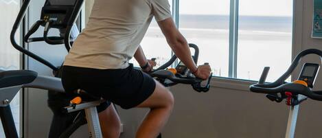 A person using an exercise bike in a room with large windows and a treadmill.