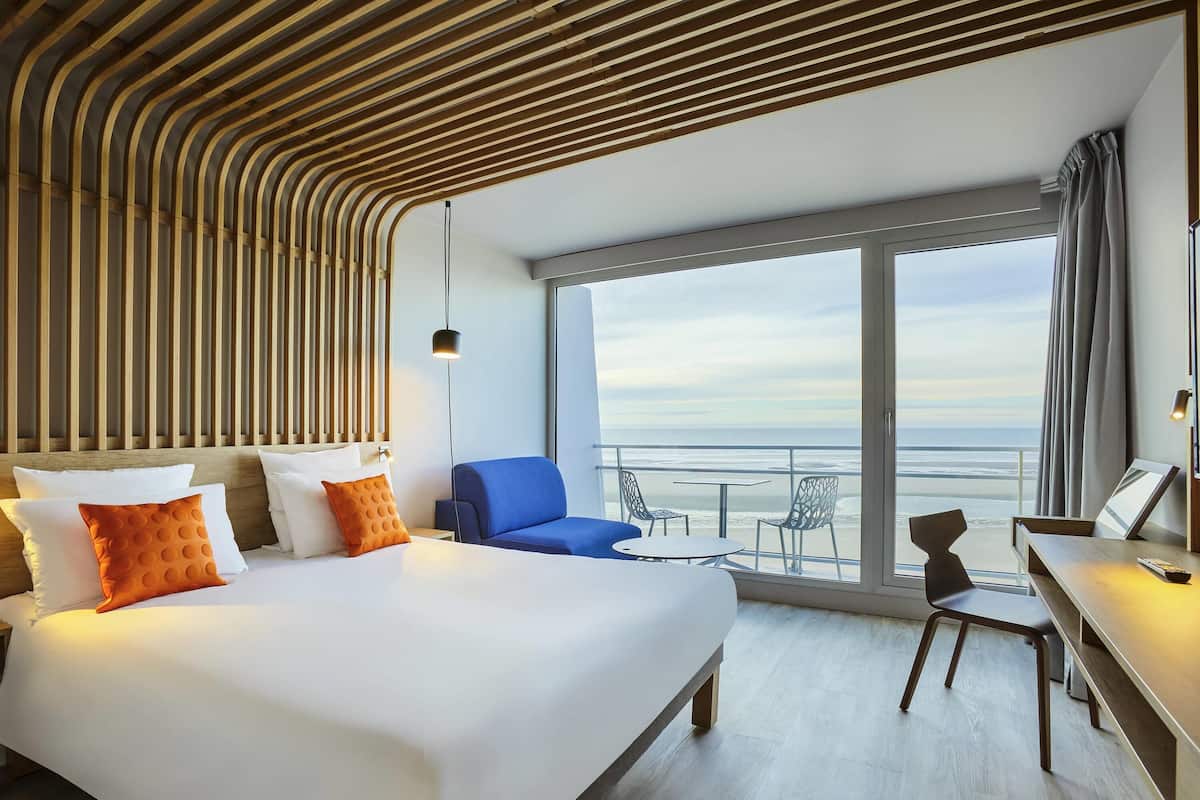 Ein Hotelzimmer mit Bett, Schreibtisch, Stuhl und einem Balkon mit Meerblick.