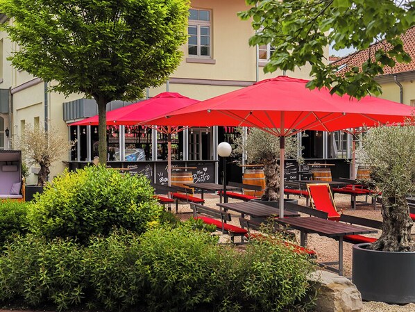 Outdoor seating with red umbrellas, a tree, and a building with a yellow facade. - Hotel Stadt Hameln (Hamelin)