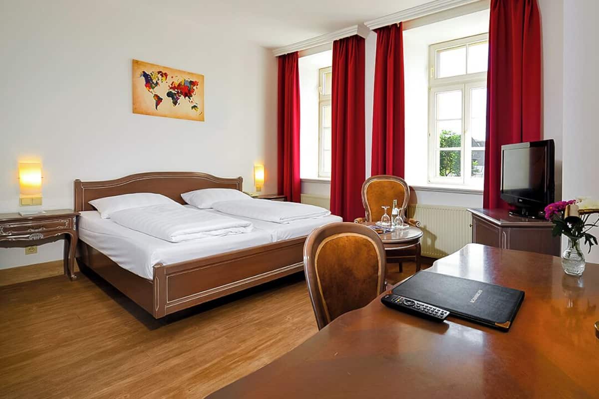 A hotel room with a double bed, a desk with a laptop, a television, and a vase with flowers.