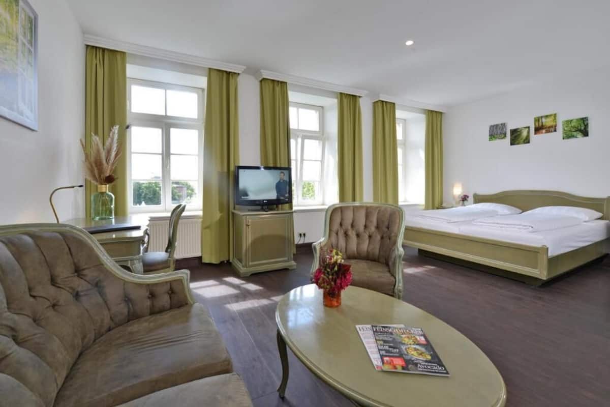 A hotel room with a bed, a sofa, a television, and a dining table.