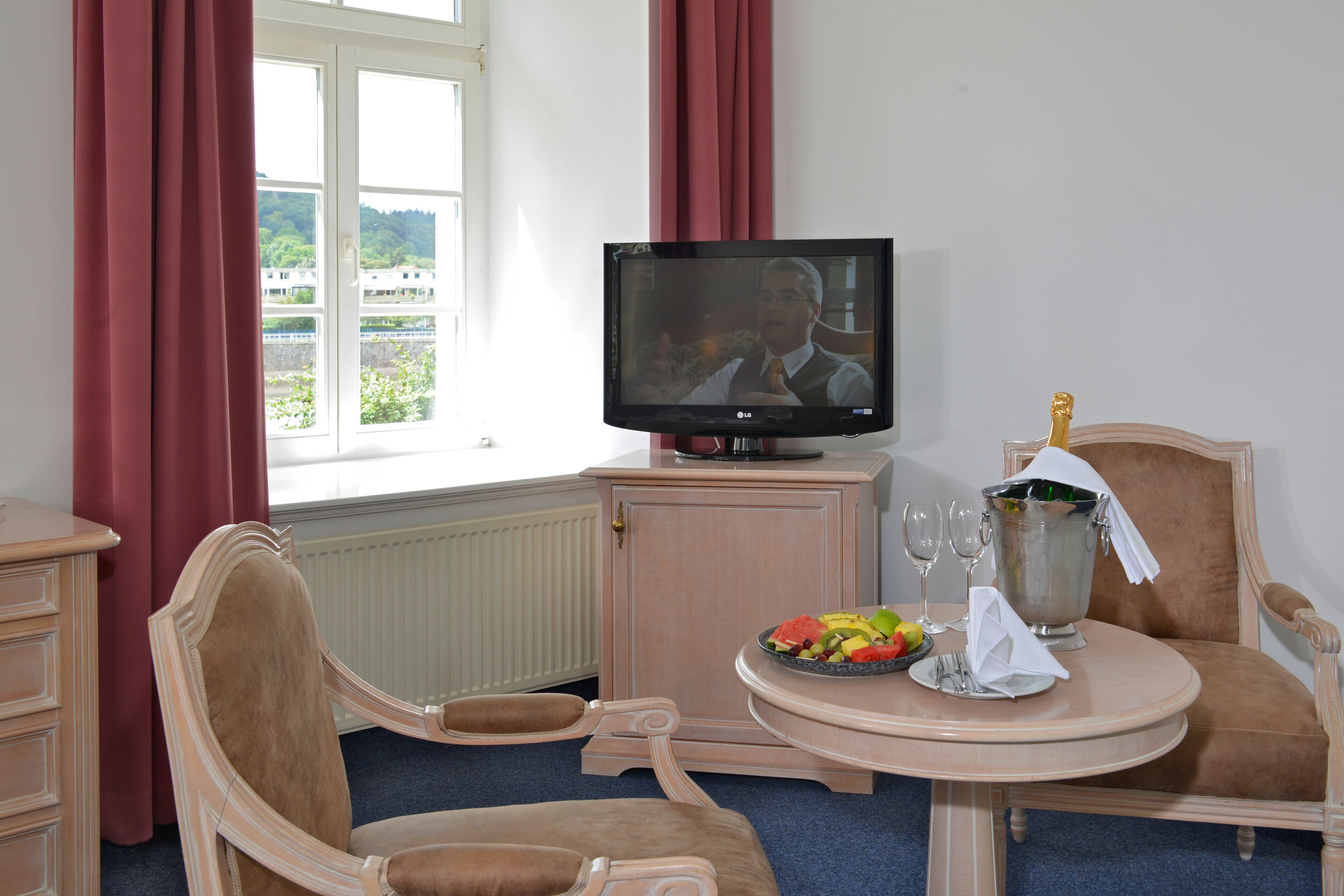 A hotel room with a television, a dining table with a fruit bowl, wine glasses, and a champagne bucket.