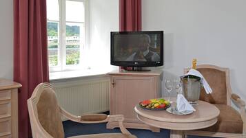 A hotel room with a television, a dining table with a fruit bowl, wine glasses, and a champagne bucket.