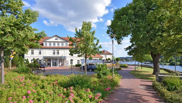 A hotel with a red-tiled roof, a paved walkway, and a river view. - Hotel Stadt Hameln (Hamelin)