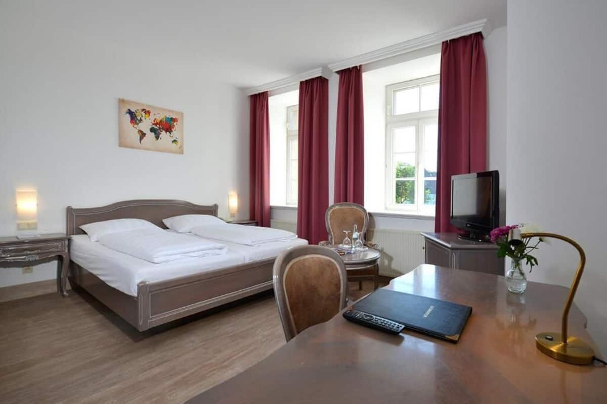 A hotel room with a bed, a desk, a chair, a TV, and a window with curtains.