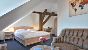 A bedroom with a bed, a sofa, a coffee table with a book and glasses, and a world map on the wall. - Hotel Stadt Hameln (Hamelin)