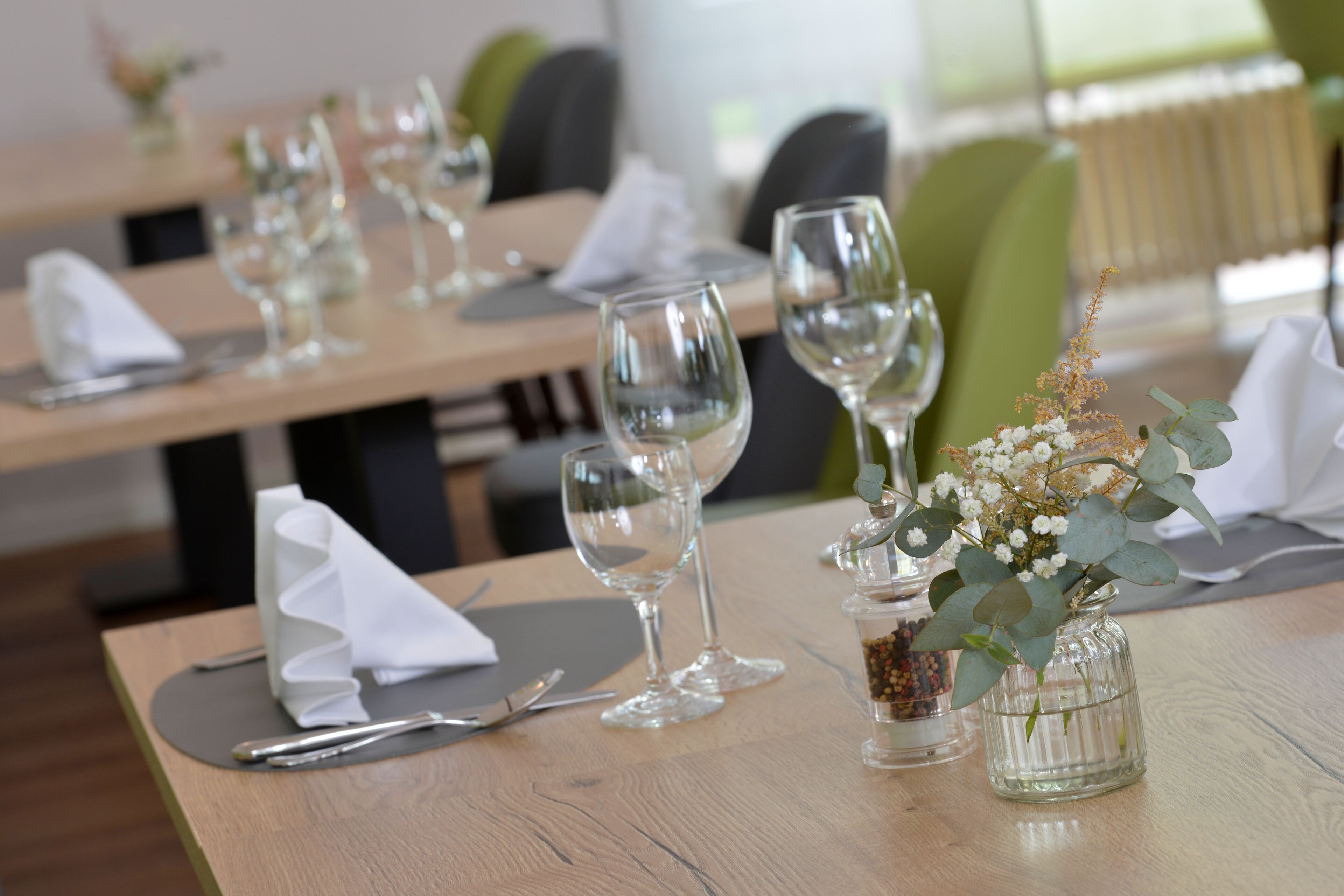 A dining table set with wine glasses, a vase with flowers, and a napkin.