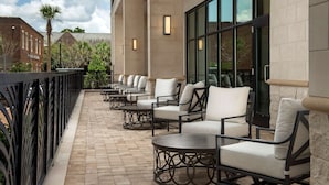 A covered outdoor seating area with multiple tables and chairs, a brick building in the background, and a palm tree. - Hilton Garden Inn Orlando Downtown (Orlando)