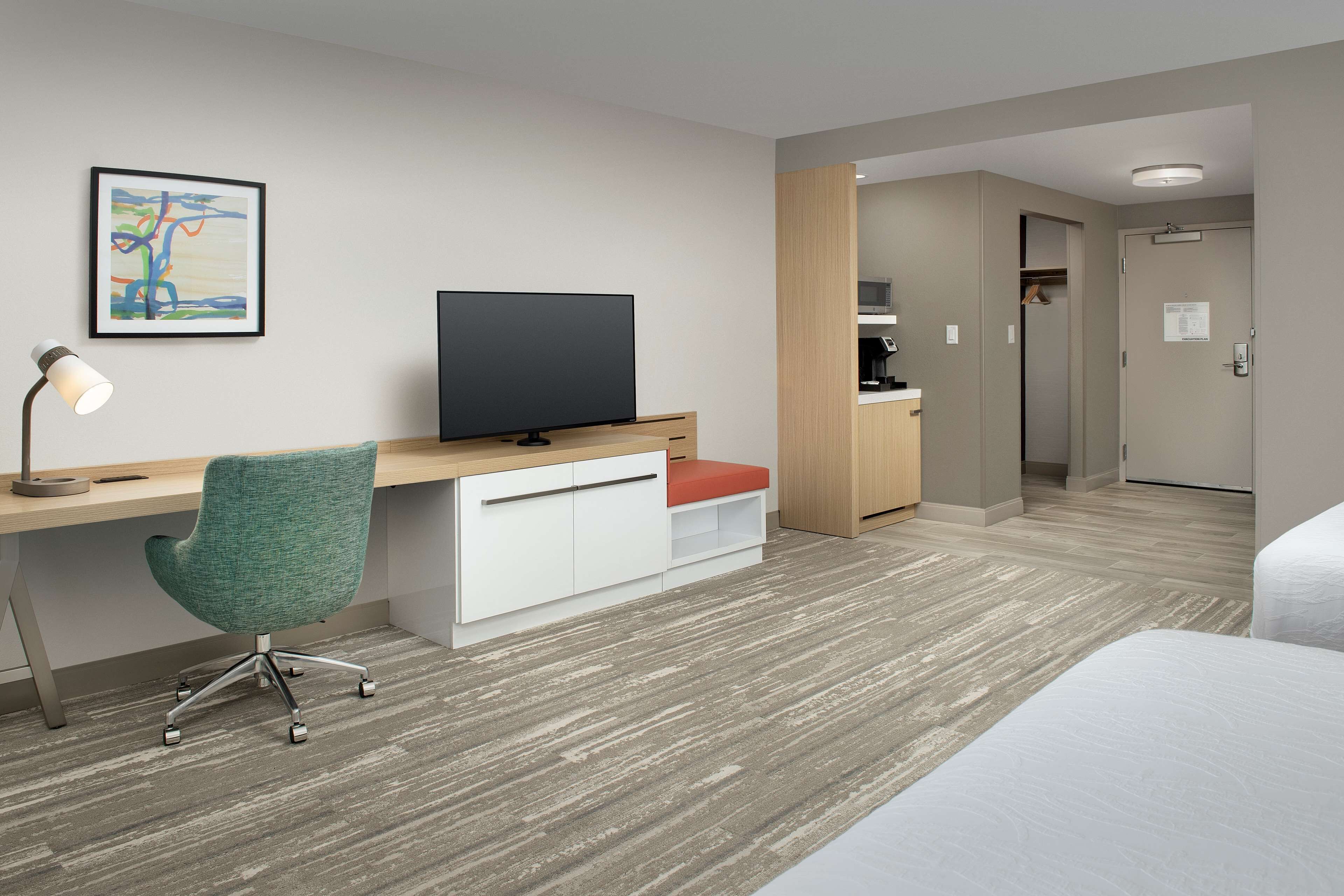 A hotel room with a wooden desk, a television, a green office chair, and a bed.
