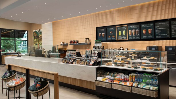 A modern coffee shop with a counter, seating area, and display cases. - Hilton Garden Inn Orlando Downtown (Orlando)