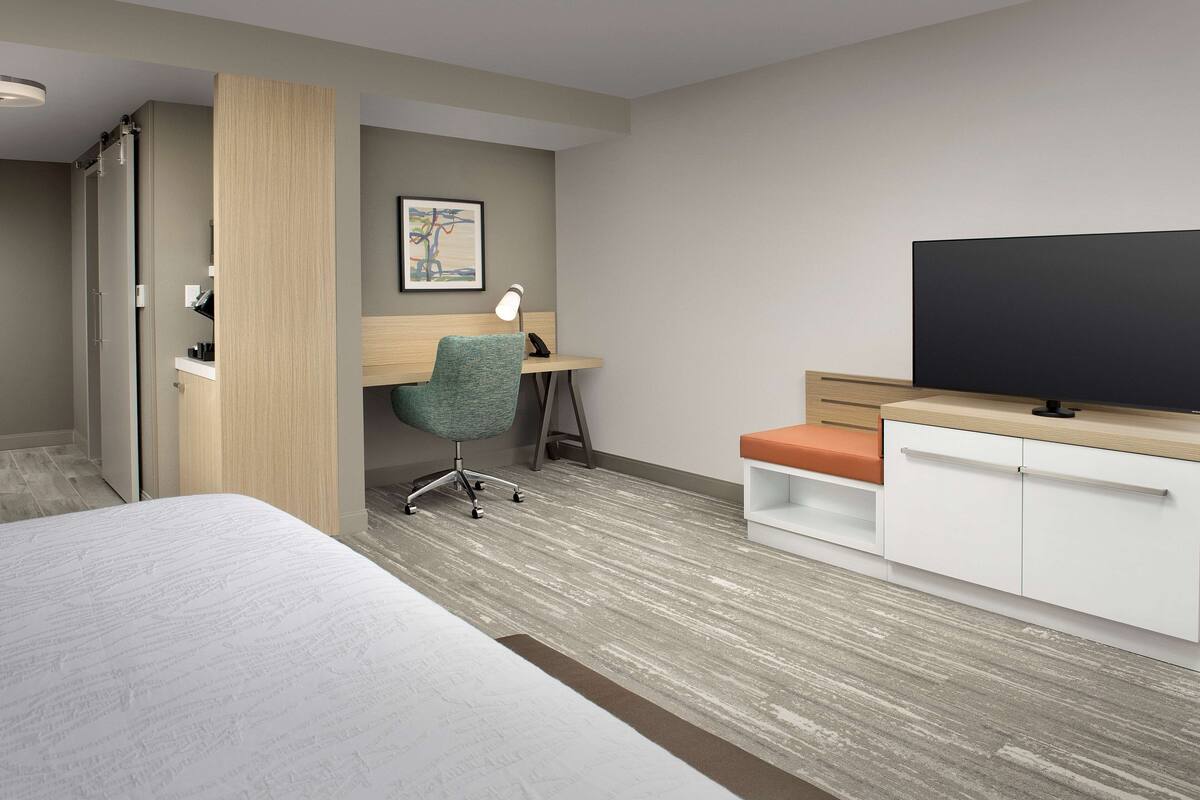 A hotel room with a bed, a desk with a chair, a television, and a wardrobe.