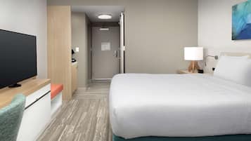 A hotel room with a bed, a TV, a desk, a chair, a nightstand, and a painting on the wall.