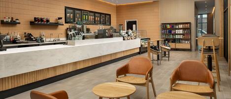 A modern cafe with a long counter, wooden chairs, and a variety of beverages and snacks displayed on shelves.