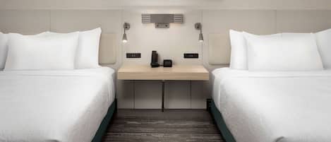 A hotel room with two beds, a desk with a phone and a lamp, and a painting on the wall.