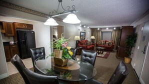 A dining area with a glass table surrounded by leather chairs, a kitchen with wooden cabinets and a black refrigerator, a red sofa, and a potted plant.