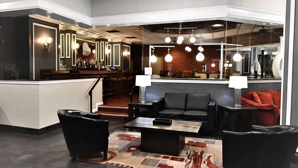 A modern lobby with a bar area, seating with a coffee table, and a large mirror reflecting the space.