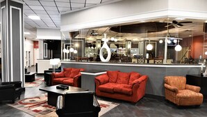 A modern interior with a seating area featuring red sofas and a patterned armchair, a coffee table, and a large mirror reflecting the room.