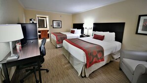A hotel room with two beds, a desk with a lamp, a television, and a chair.