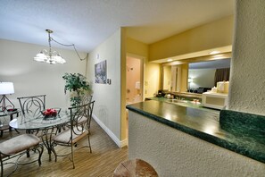 A modern kitchen with a green marble countertop, a dining area with a glass table and metal chairs, and a hallway leading to a bathroom.