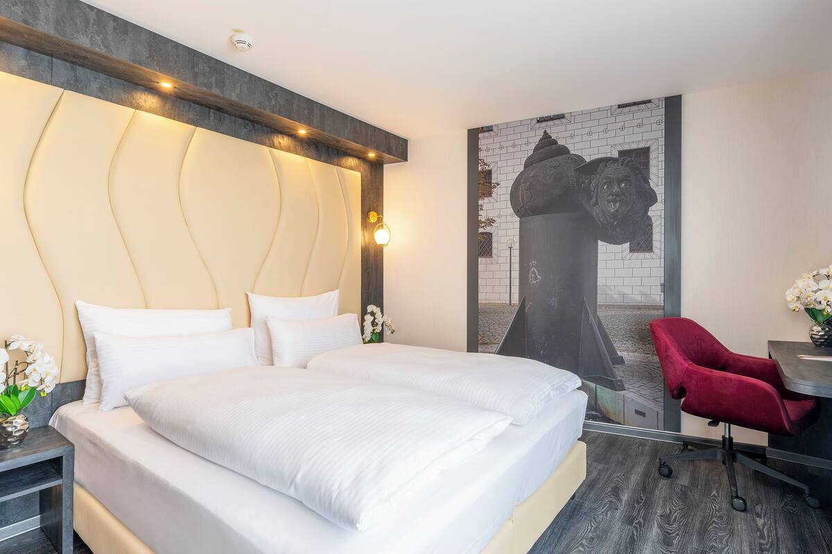 Ein modernes Hotelzimmer mit einem großen Bett, einem roten Sessel, einem Schreibtisch und einem an der Wand montierten Fernseher.