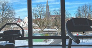 A room with a large window overlooking a cityscape, including a church spire and residential buildings. - PLAZA Premium Parkhotel Neu-Ulm (Neu-Ulm)