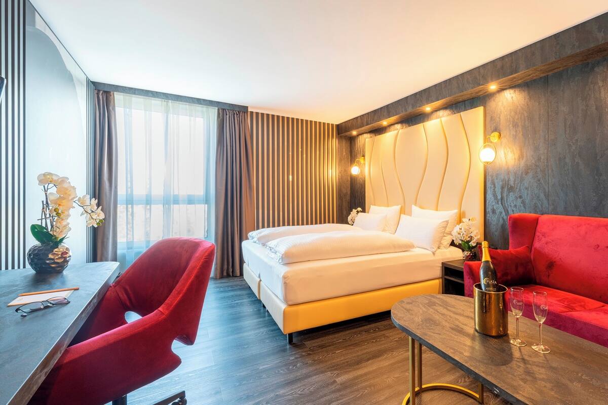 Ein modernes Hotelzimmer mit einem Bett, einem roten Sofa und einem Schreibtisch mit einer Champagnerflasche.