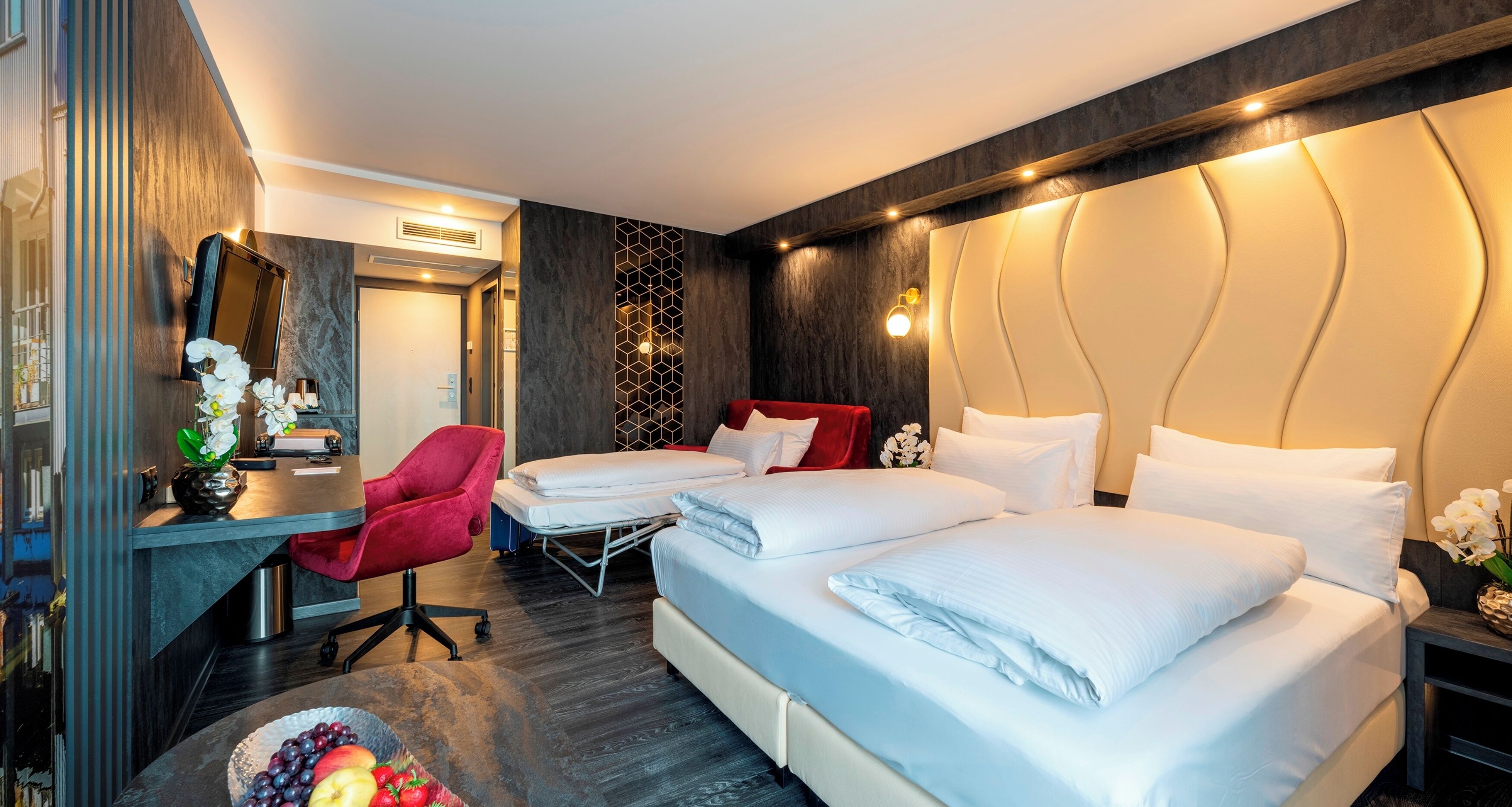Een hotelkamer met twee bedden, een bureau, een stoel en een kleine tafel met fruit.
