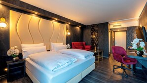 A modern hotel room with a large bed, a desk, a red chair, and a mirror.