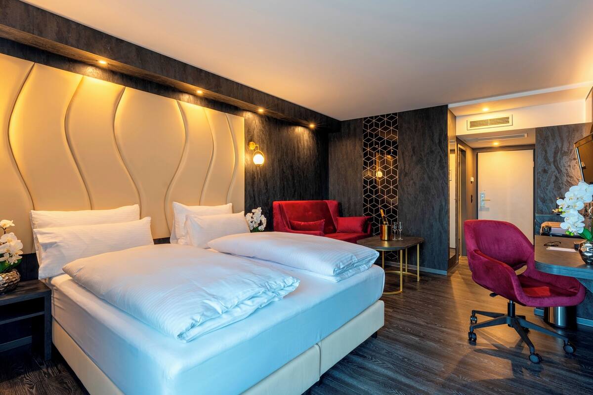 Ein modernes Hotelzimmer mit einem großen Bett, einem Schreibtisch, einem roten Sessel und einem Spiegel.
