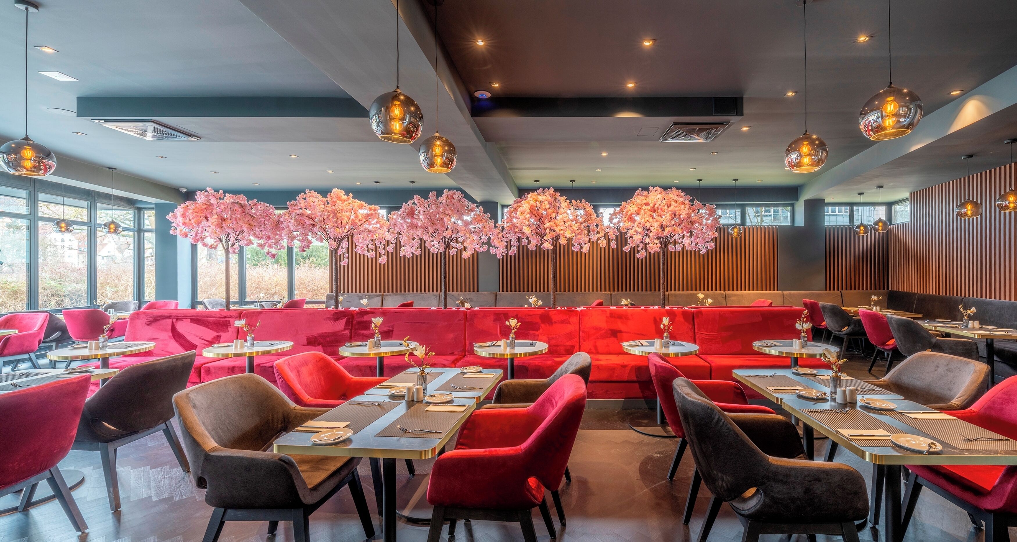 A modern restaurant with red seating, round tables, and decorative hanging lights.