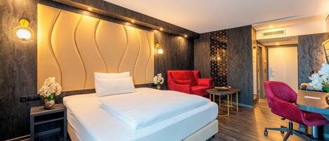 Una camera d'albergo moderna con un letto grande, una scrivania con una sedia e una poltrona rossa.